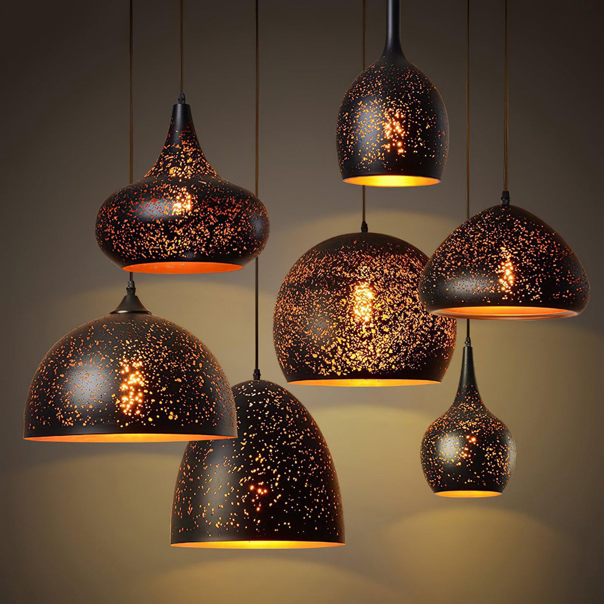 Seven Clérachic pendants in teardrop, dome and bell shapes grouped at varied heights, each lit with a speckled pattern and a gold lining.