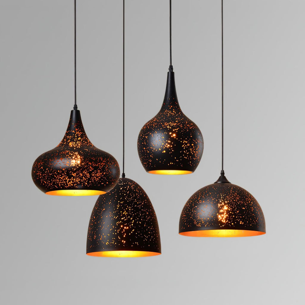 Four Clérachic pendants with perforated black shades and gold interiors, hung at different heights against a plain grey backdrop.