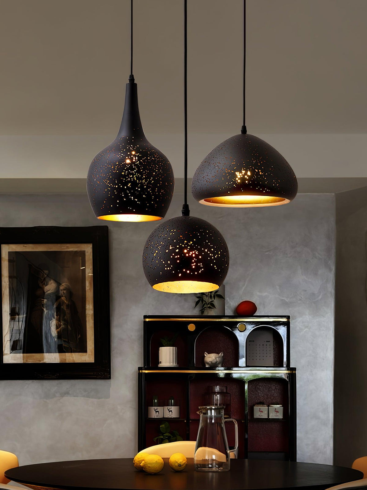 Three Clérachic pendants, a teardrop, a round dome and a wide dome, at staggered heights above a dark table with lemons, in a grey room.
