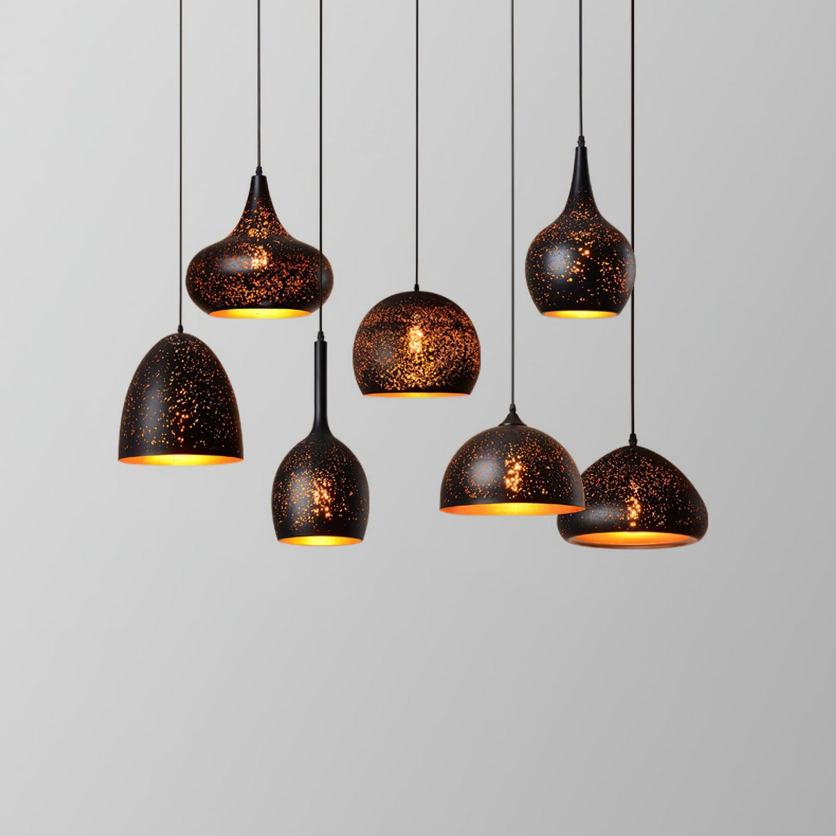 Seven Clérachic pendants in assorted shapes at different lengths, each with a speckled black shade, against a pale grey backdrop.