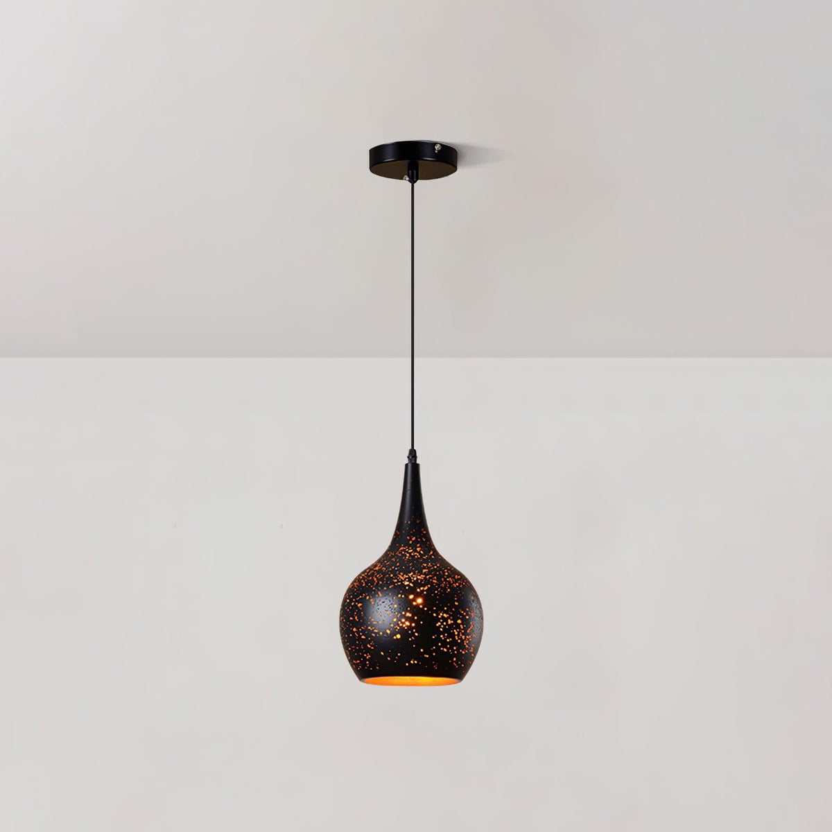 Teardrop Clérachic pendant with a black perforated shade and a gold interior, hanging from a round ceiling plate against a white wall.