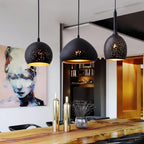 Three Clérachic pendants over a polished wood counter, with a painted portrait and gold bottles in a modern dining space behind them.
