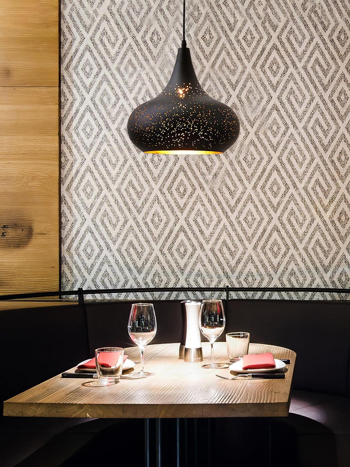 Clérachic teardrop pendant above a restaurant booth with a set table, against a wall of geometric grey and white wallpaper.