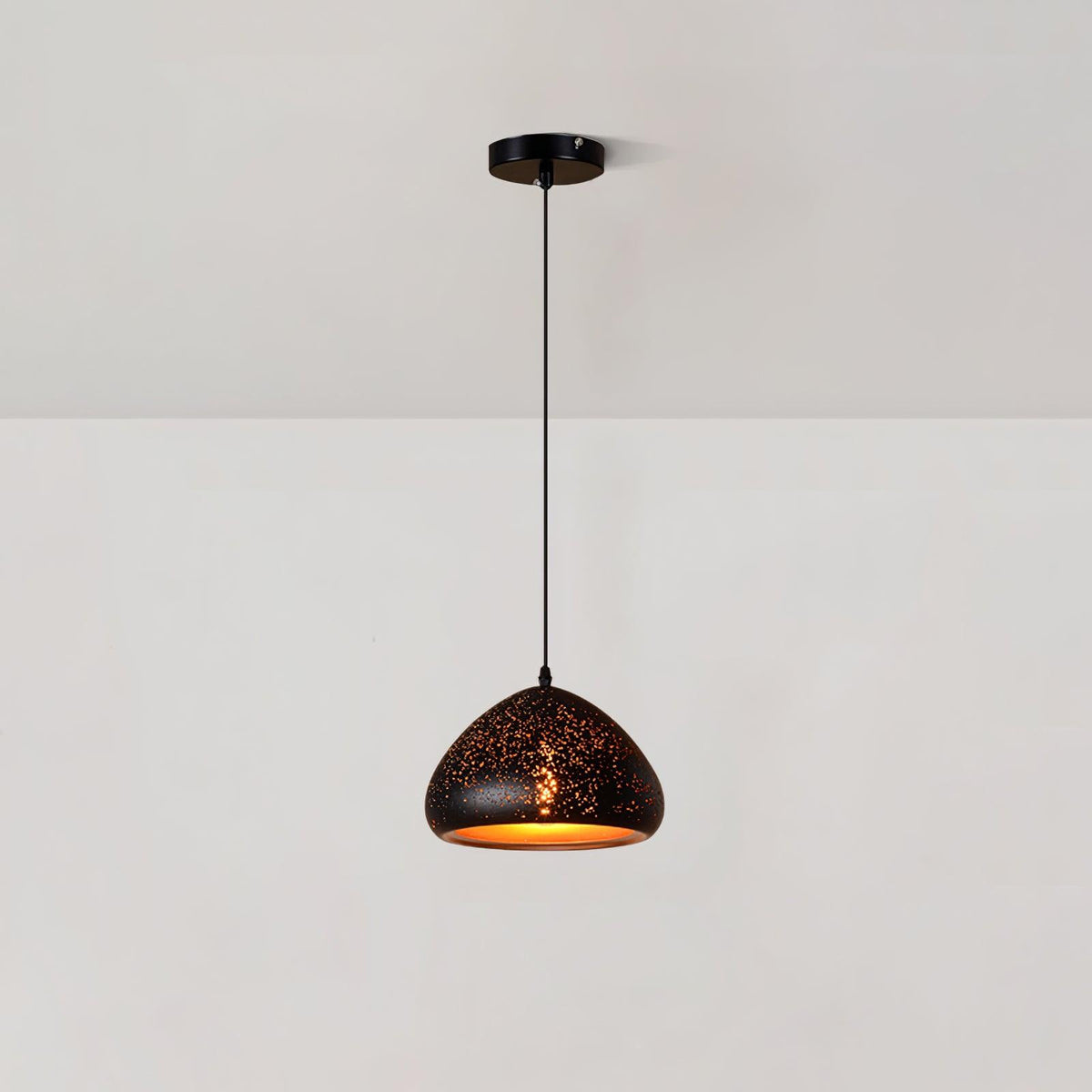 Low, wide Clérachic pendant with a rounded black shade dotted with small perforations, hanging from a ceiling plate on a white wall.