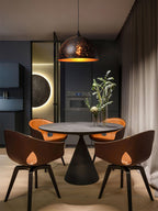 Clérachic domed pendant above a round dark dining table with four tan chairs, in a moody room with a glowing wall circle.