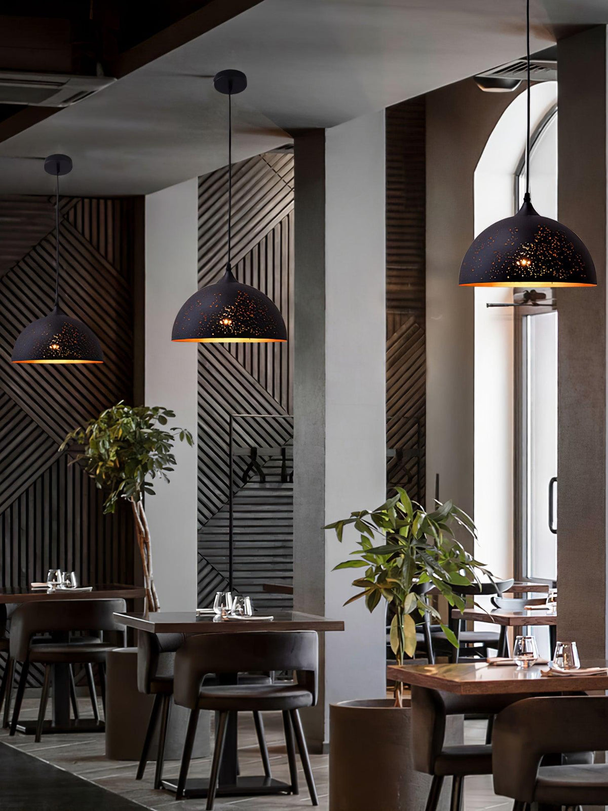 Clérachic dome pendants hanging at different heights in a restaurant with slatted wood panelling, plants and set tables below.