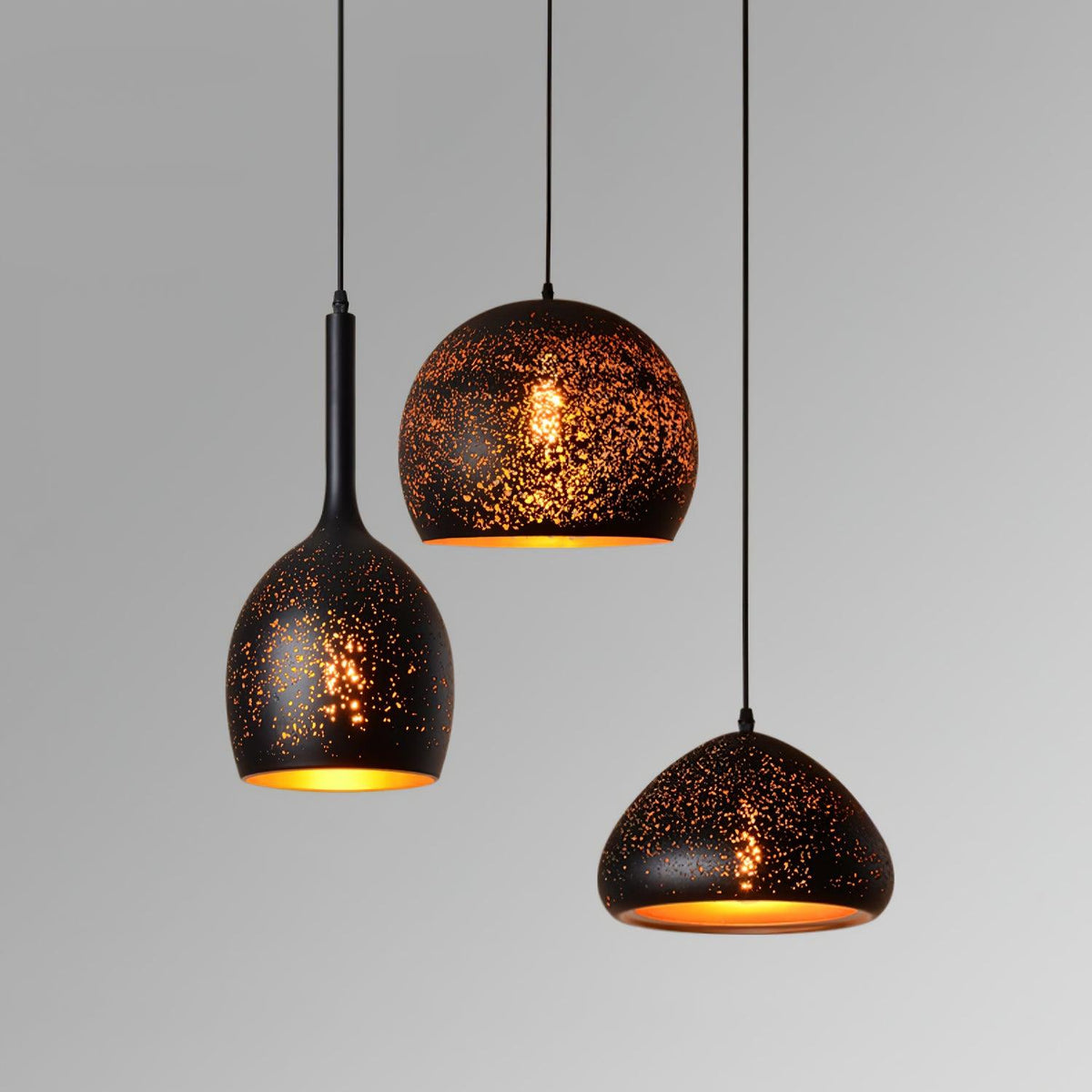 Three Clérachic pendants of different shapes and drops against a pale grey backdrop, each with a perforated black shade and gold lining.