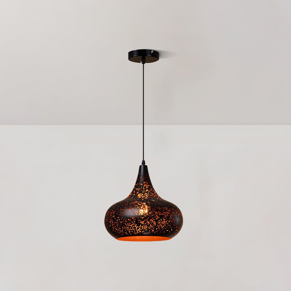 Clérachic pendant with a rounded teardrop shade and a perforated black surface, hanging from a ceiling plate against a pale wall.
