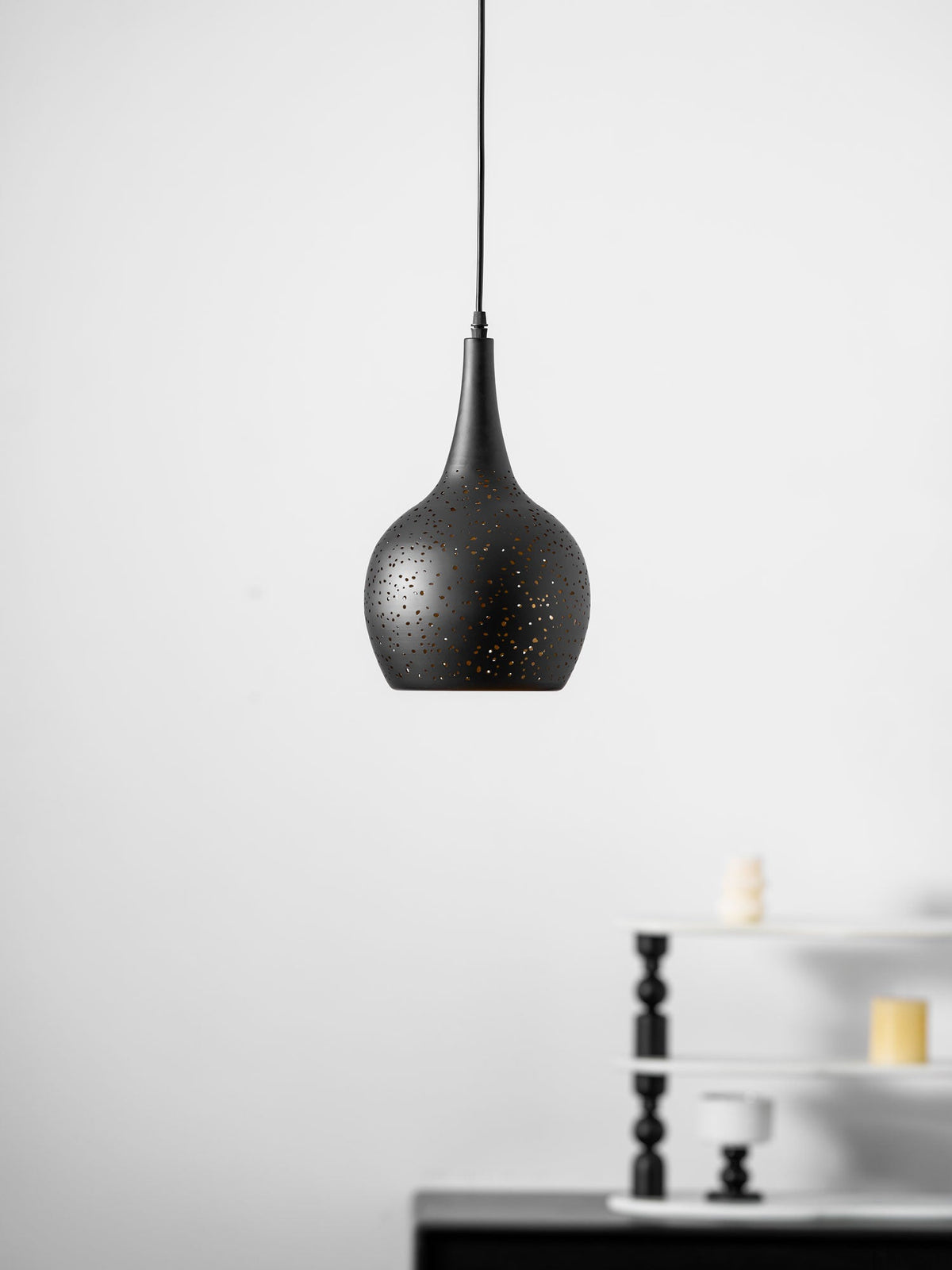 Larger view of the black teardrop Clérachic pendant on its thin cord, with a black sideboard and a small white shelf behind.