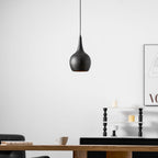 Black teardrop Clérachic pendant with fine perforations, hanging in front of a white wall and a black sideboard topped with candles.