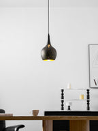 Teardrop Clérachic pendant with a faint gold glow showing through its perforations, in a white room with a wooden table beneath.