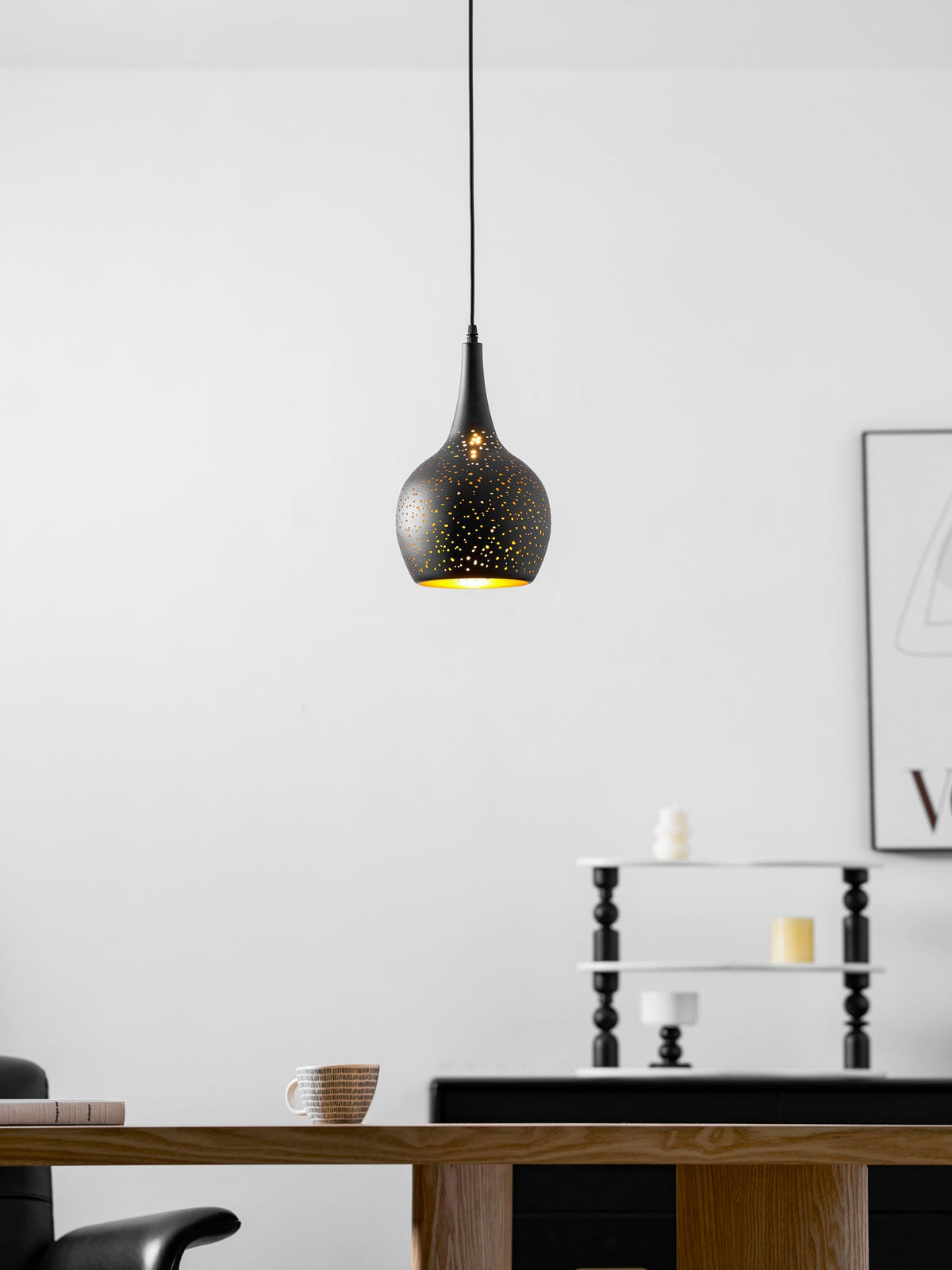 Teardrop Clérachic pendant with a faint gold glow showing through its perforations, in a white room with a wooden table beneath.