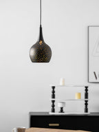 Teardrop Clérachic pendant hanging in front of a white wall, a framed print and a black sideboard behind and a wooden table below.