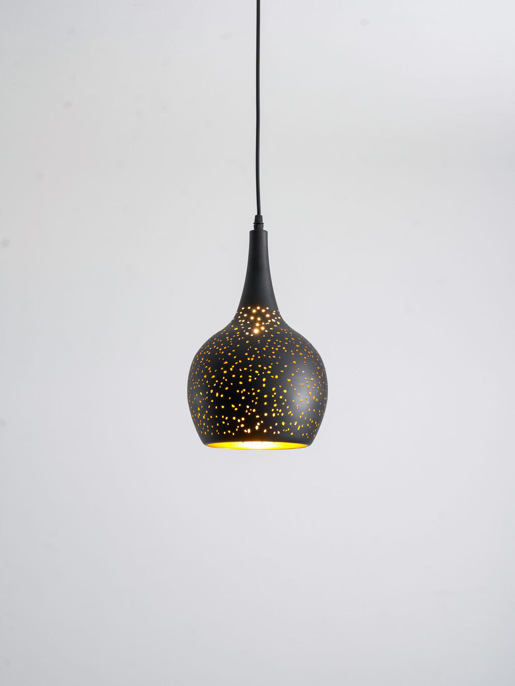 Teardrop Clérachic pendant with a perforated black shade, its gold interior just visible, hanging against a pale grey backdrop.