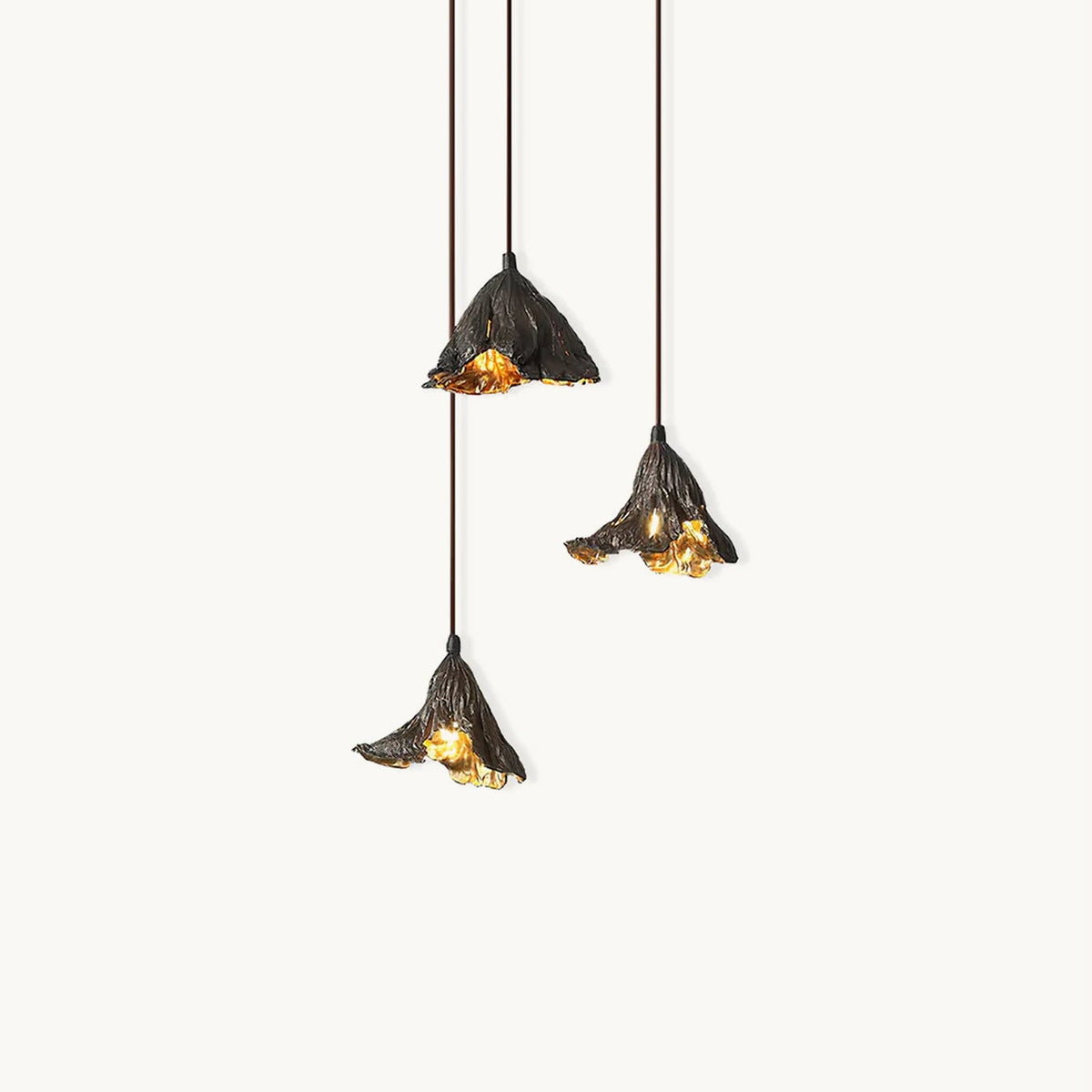 Three Clérachic pendants with crinkled dark metal shades and gold-lit insides hang at different heights on a white backdrop.
