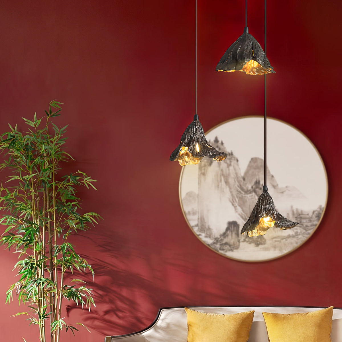 Three Clérachic pendants in dark metal with gold interiors hang against a red wall with a round landscape painting and bamboo.