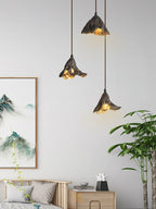 Three Clérachic pendants hang beside a landscape scroll on a white wall, above a daybed with grey cushions and a tall plant.