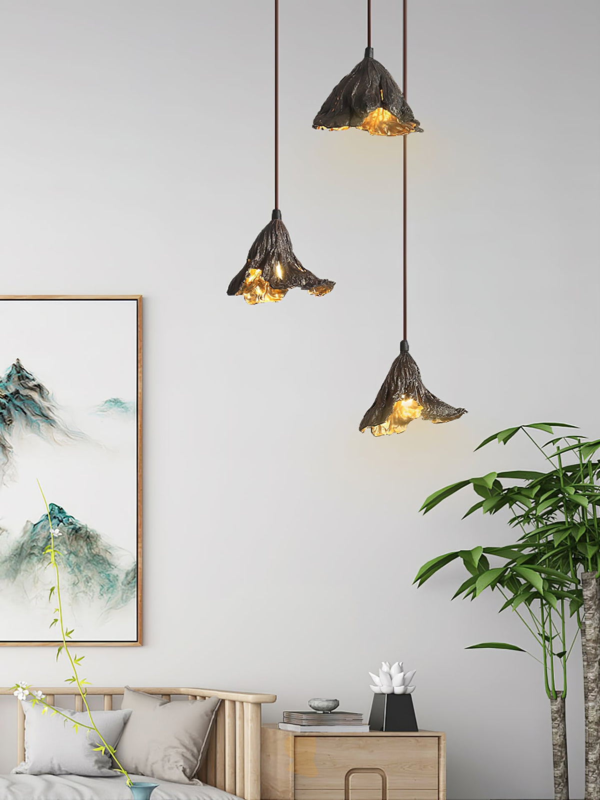 Three Clérachic pendants hang beside a landscape scroll on a white wall, above a daybed with grey cushions and a tall plant.