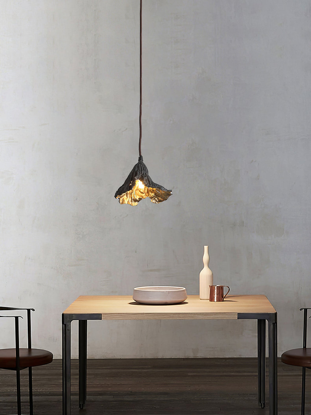 A single Clérachic pendant with a crinkled black shade hangs above a pale wood table with a pink bowl and a tall white vase.