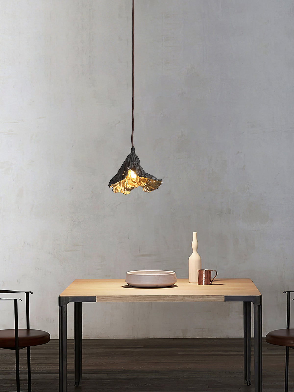 A single Clérachic pendant with a crinkled black shade hangs above a pale wood table with a pink bowl and a tall white vase.