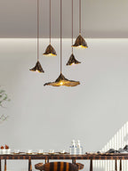 Five Clérachic pendants with flared leaf shades hang at varied heights above a long table in a pale, sunlit room.