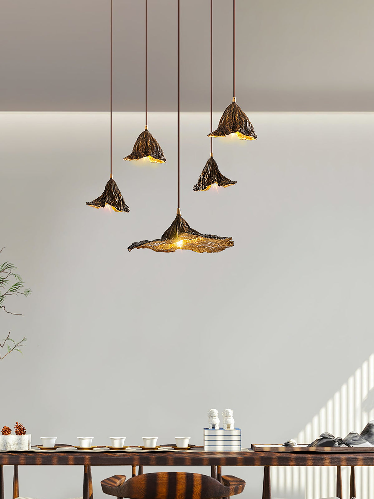 Five Clérachic pendants with flared leaf shades hang at varied heights above a long table in a pale, sunlit room.