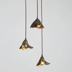Three Clérachic pendants with black outer shades and gold interiors hang at different drops against a light grey backdrop.