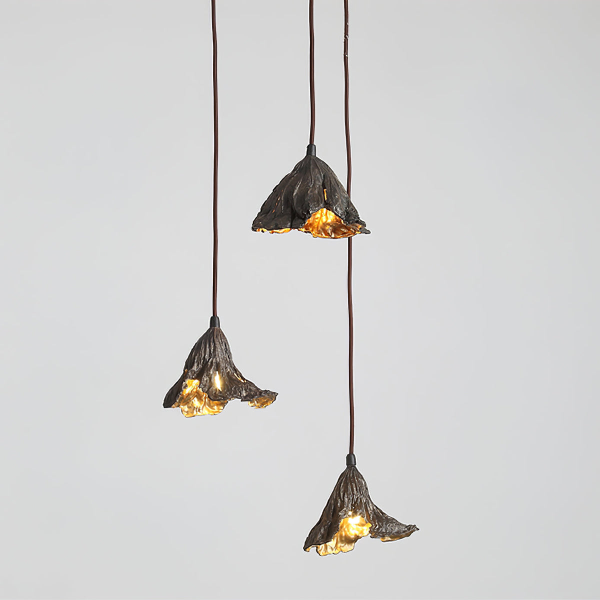 Three Clérachic pendants with black outer shades and gold interiors hang at different drops against a light grey backdrop.