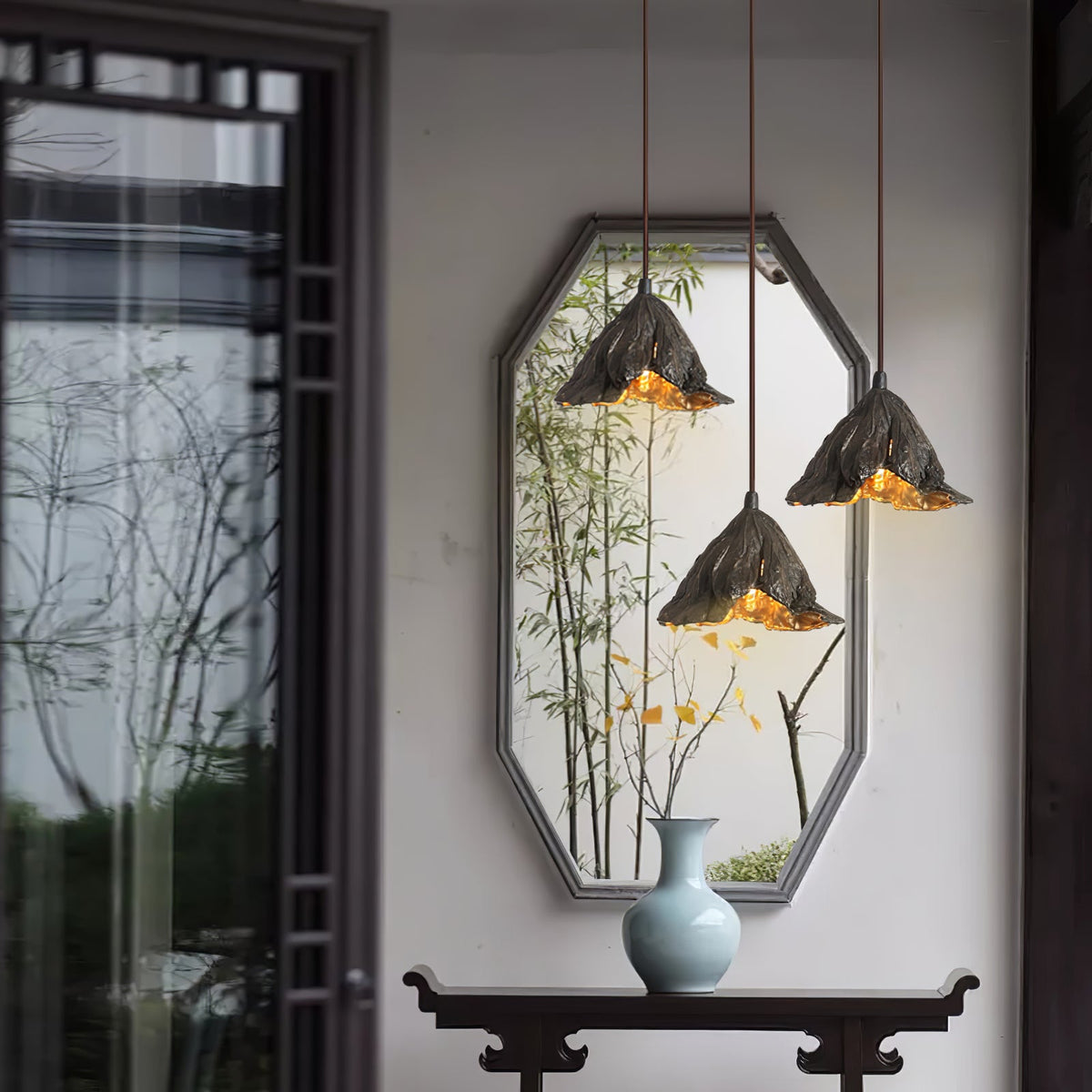 Three Clérachic pendants hang in front of an octagonal mirror reflecting bamboo, beside a glazed door with a dark frame.