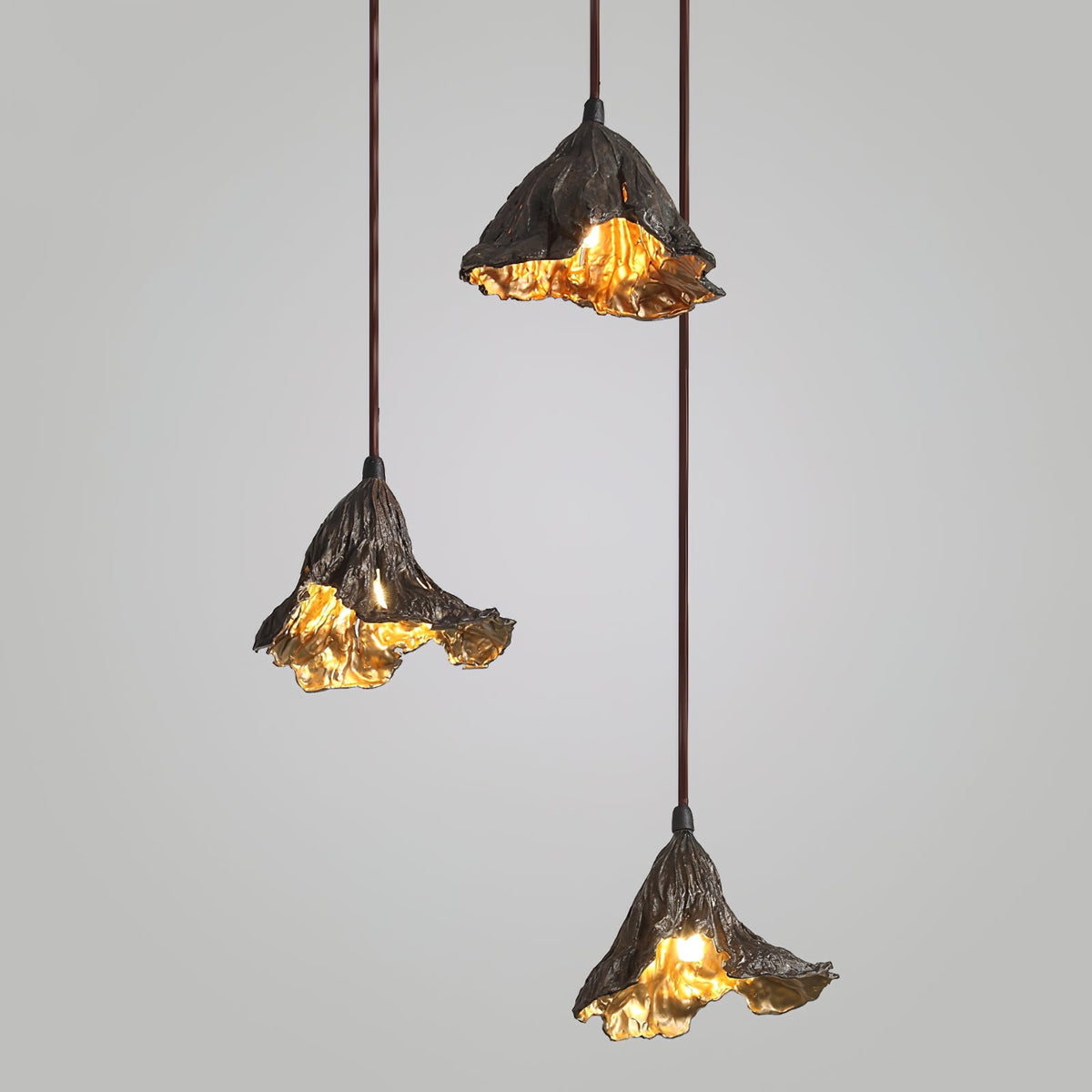 Three Clérachic leaf-shaped pendants hang at staggered heights against a soft grey backdrop, each warmly lit inside.