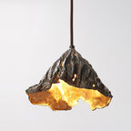 Close view of the pitted dark metal outside and gold inside of this Clérachic pendant, with light showing through small holes.