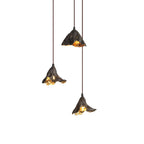 Three small Clérachic pendants of dark metal hang at staggered heights on a white backdrop, lit gold within.