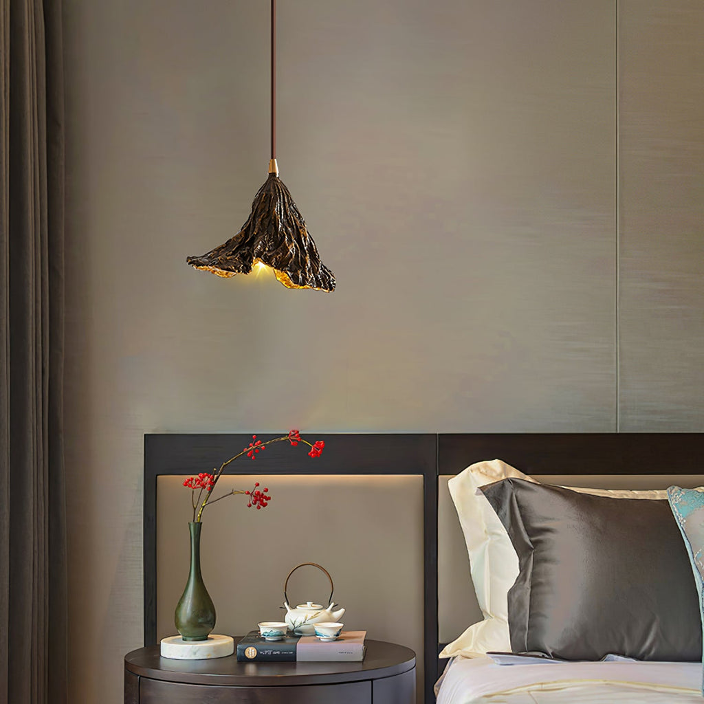A Clérachic pendant with a ruffled black shade hangs in a bedroom above a round bedside table with a vase and a tea set.