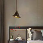 A Clérachic pendant with a ruffled black shade hangs in a bedroom above a round bedside table with a vase and a tea set.