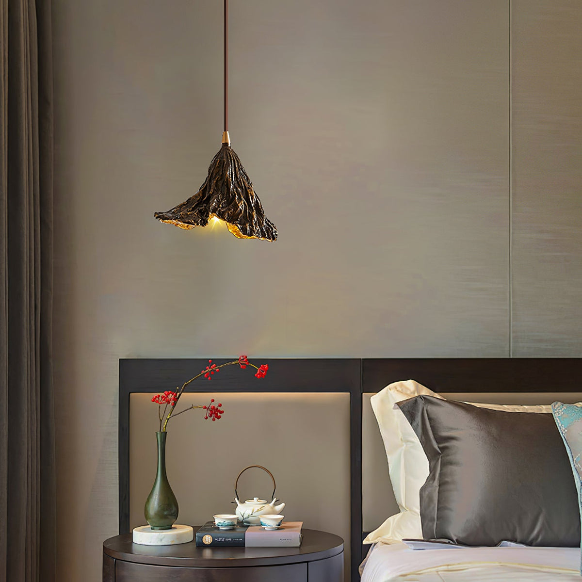 A Clérachic pendant with a ruffled black shade hangs in a bedroom above a round bedside table with a vase and a tea set.