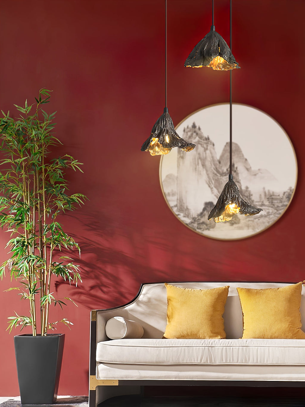 Three Clérachic pendants hang before a red wall with a round landscape painting, above a cream sofa with mustard cushions.