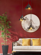 Three Clérachic pendants hang before a red wall with a round landscape painting, above a cream sofa with mustard cushions.
