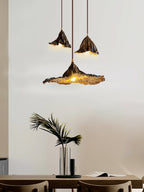 Three Clérachic pendants in dark metal hang above a plant and a dark table, the largest with a wide, flat flared shade.