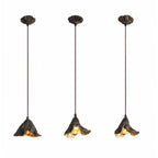 Three Clérachic pendants with leaf-shaped canopies and long cords hang side by side, each lit gold, on a white backdrop.