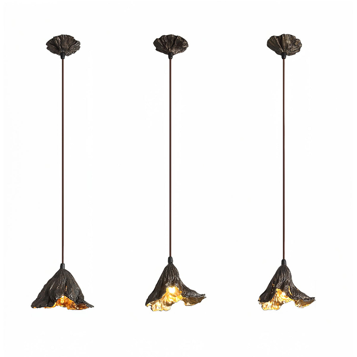 Three Clérachic pendants with leaf-shaped canopies and long cords hang side by side, each lit gold, on a white backdrop.
