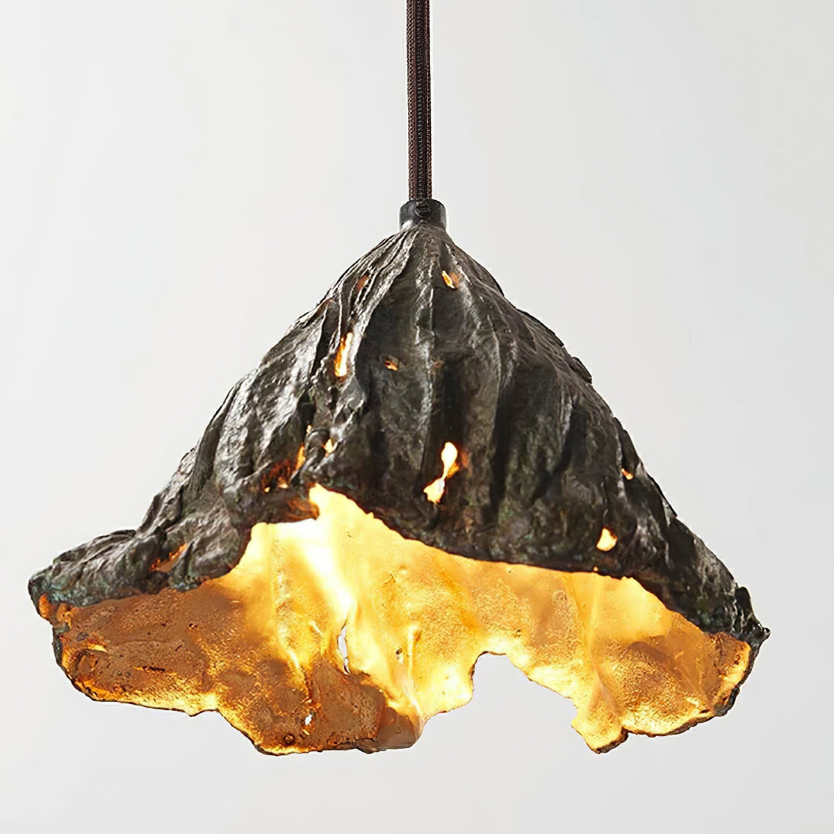 Close view of the pitted black outside and glowing gold inside of this Clérachic pendant, with light through small holes.