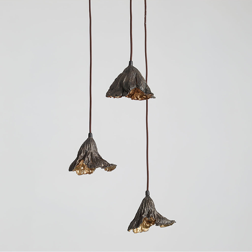 Three Clérachic pendants hang at staggered heights against a soft grey backdrop, their gold interiors lit.