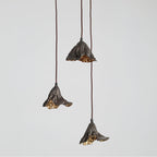 Three Clérachic pendants hang at staggered heights against a soft grey backdrop, their gold interiors lit.