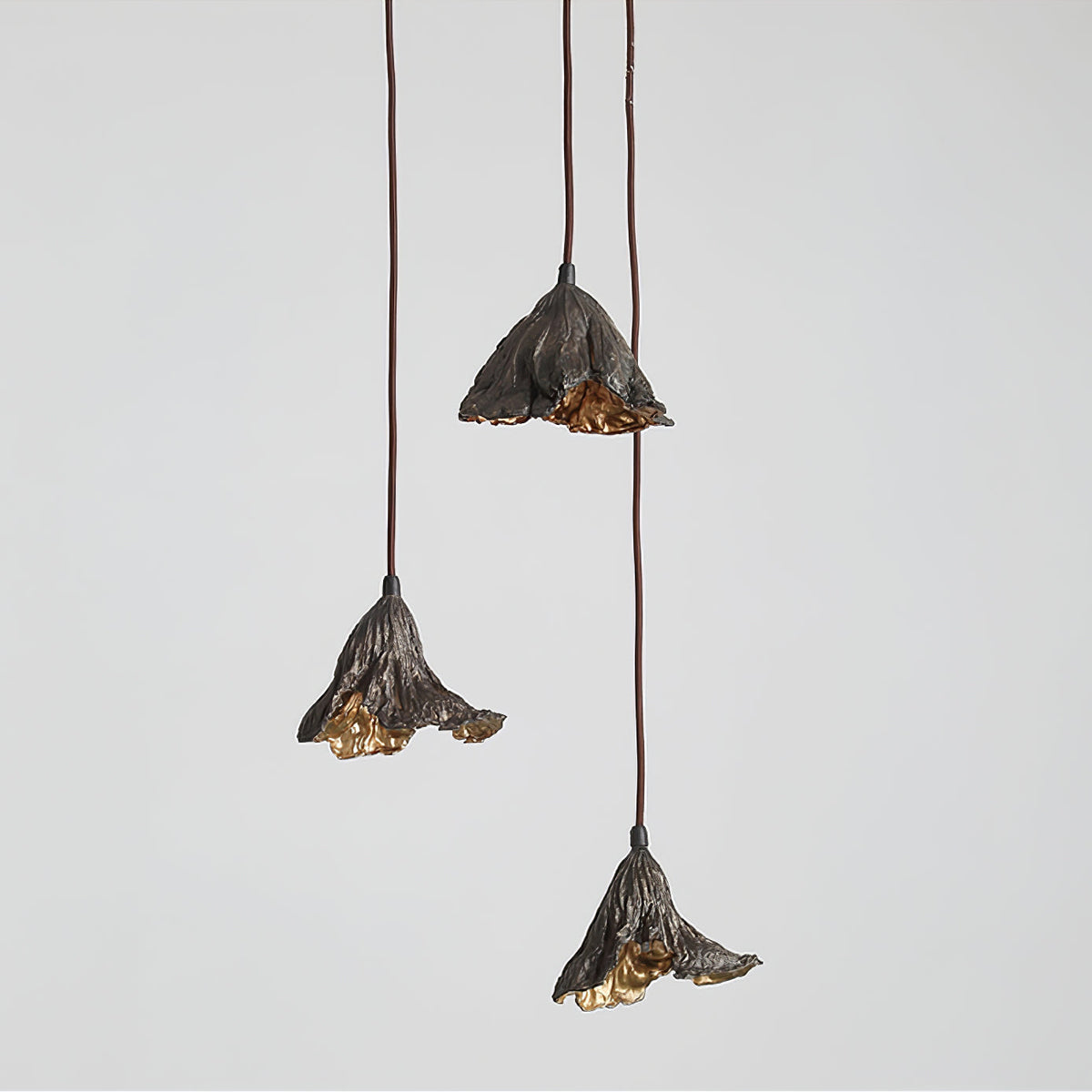 Three Clérachic pendants hang at staggered heights against a soft grey backdrop, their gold interiors lit.