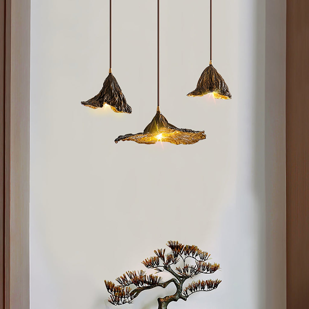 Three Clérachic pendants, one with a wide flat shade, hang beside a white wall with a dark frame and a bonsai below.