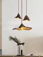Three Clérachic pendants hang in a pale room, the lowest with a wide flat shade, above a vase of palm leaves on a table.