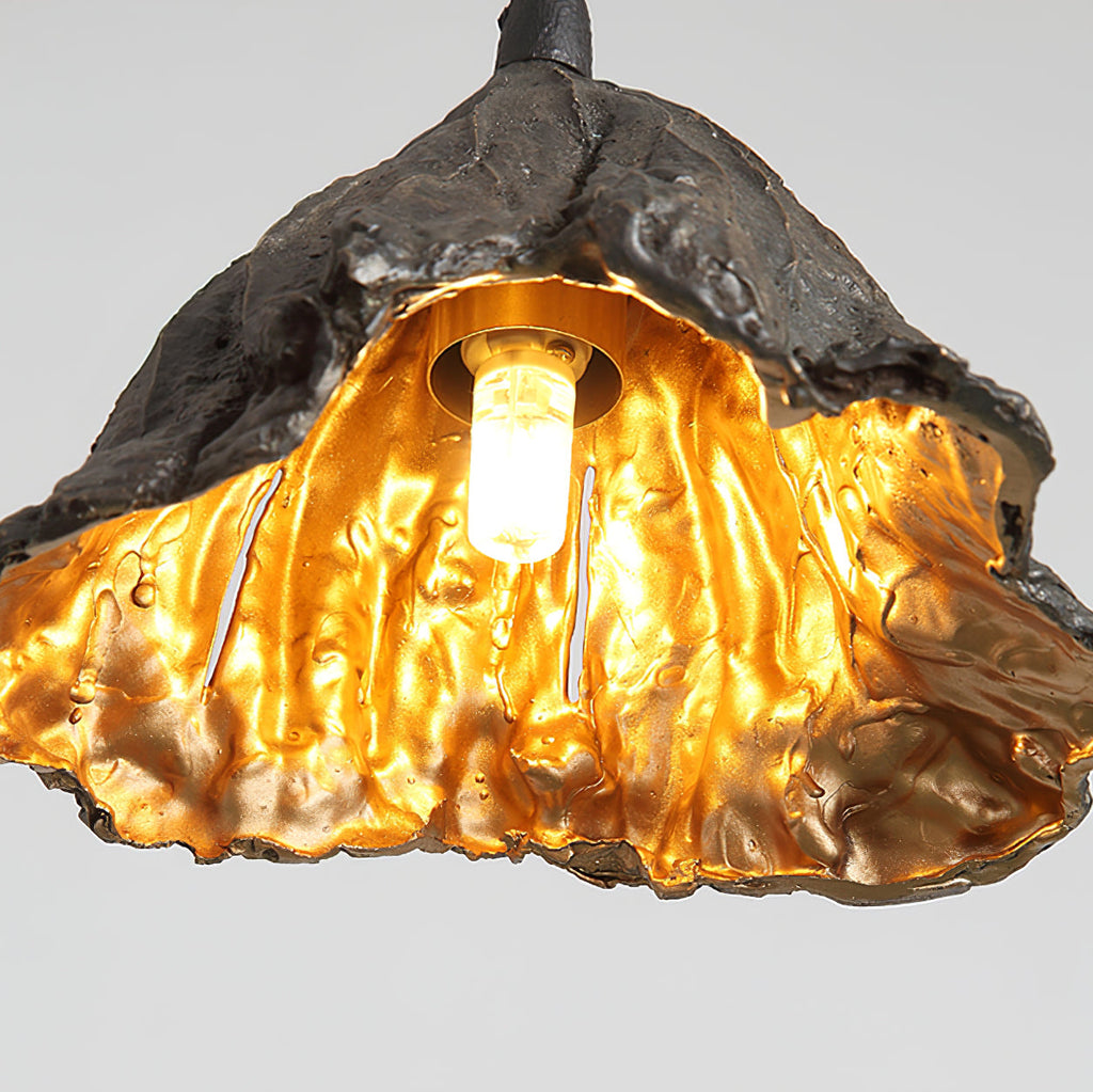Close view of the glowing bulb and gold interior of this Clérachic pendant, with a rough black exterior.