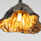 Close view of the glowing bulb and gold interior of this Clérachic pendant, with a rough black exterior.