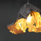Close view of a lit bulb inside this Clérachic pendant's gold interior, set against a dark grey backdrop.