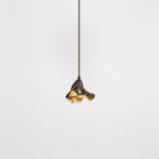 A small Clérachic pendant with a dark ruffled shade and gold interior hangs from a thin cord against a pale backdrop.